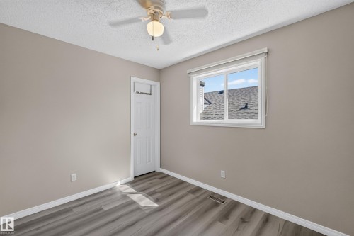 Neutral-toned room featuring a ceiling fan with integrated lighting, wood-finish flooring, a white trim package, and a white window with a roller blind - 2327 37B Avenue, Edmonton, AB 