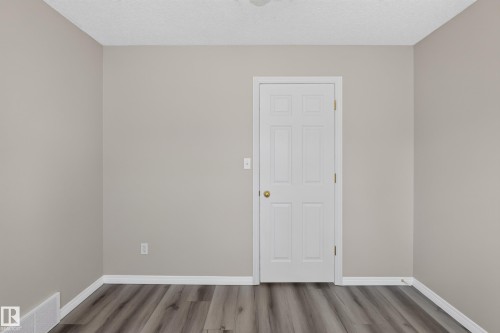 Interior room with neutral wall color, wood-finish flooring, white baseboards, and a six-panel door with brass hardware - 2327 37B Avenue, Edmonton, AB 