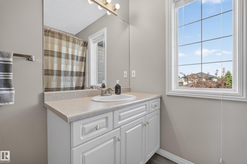 Bathroom featuring a white vanity with a light-toned countertop, an integrated sink, a large wall-mounted mirror, and a multi-bulb vanity light fixture - 2327 37B Avenue, Edmonton, AB 