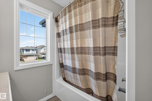 White-framed window with grid pattern above a bathtub, featuring a striped shower curtain, white subway tile surround, and chrome fixtures - 2327 37B Avenue, Edmonton, AB 