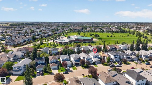 Aerial perspective showcasing the subject property within a residential development, featuring a green space and a large building with a circular roof structure - 2327 37B Avenue, Edmonton, AB 