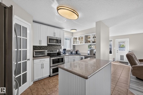 Kitchen featuring white cabinetry, stainless steel appliances, a stone-finish countertop island, and tile flooring - 2327 37B Avenue, Edmonton, AB 