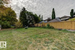 Expansive backyard featuring a natural grass lawn, mature perimeter trees, and a wooden privacy fence - 