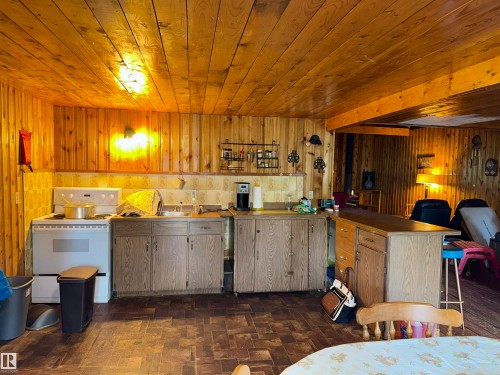 Kitchen area featuring wood-paneled walls and ceiling, a white freestanding range, a stainless steel sink, wood-finish cabinetry - 208 60118 Secondary Highway 867, Rural St. Paul County, AB - Indoor Photo Showing Kitchen