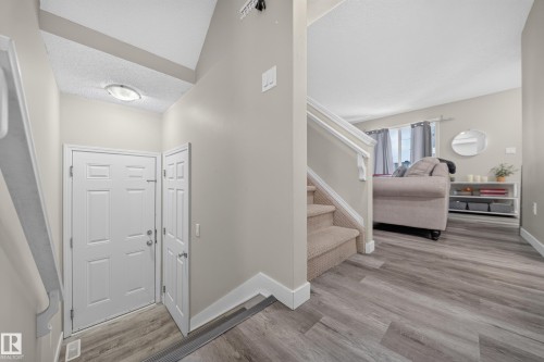 Entry foyer featuring a white paneled door, vaulted ceiling, and wood-finish flooring - 59 2503 24 Street, Edmonton, AB 