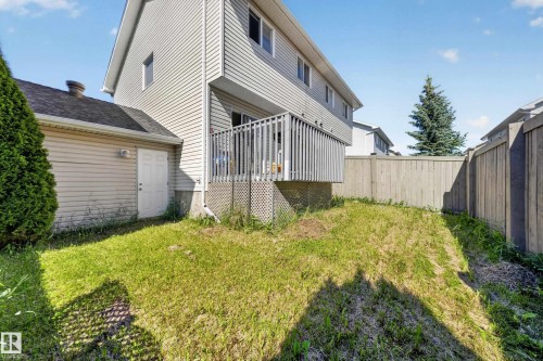 Rear exterior showcasing a raised wooden deck with lattice skirting, an attached single-story structure with a white entry door, and a partially fenced yard - 59 2503 24 Street, Edmonton, AB 