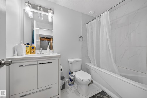 Bathroom featuring a white vanity with integrated sink, rectangular mirror, and wall-mounted light fixture - 59 2503 24 Street, Edmonton, AB 
