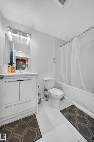 Modern bathroom featuring a white vanity with integrated sink, contemporary lighting, white subway-style shower wall tile, a built-in bathtub, and large format floor tiling - 59 2503 24 Street, Edmonton, AB 