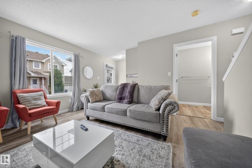 Spacious living area featuring wood-finish flooring, light grey wall paint, a large picture window, and visible staircase - 59 2503 24 Street, Edmonton, AB 