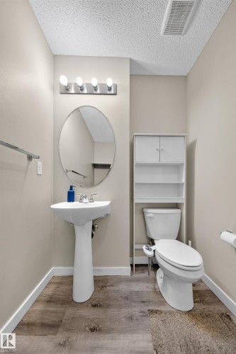 Pedestal sink with an oval mirror, modern vanity lighting, and wood-finish flooring - 59 2503 24 Street, Edmonton, AB 