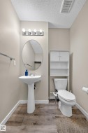 Pedestal sink with an oval mirror, modern vanity lighting, and wood-finish flooring - 