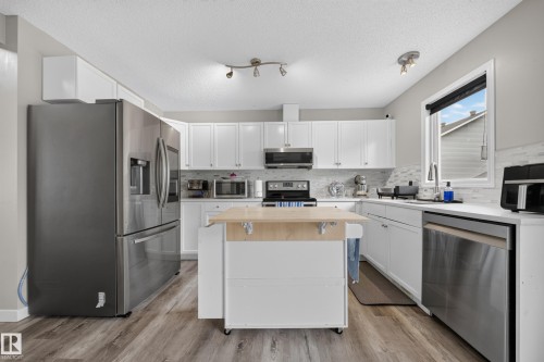 Kitchen featuring white cabinetry, stainless steel appliances, white countertops, and wood-finish flooring - 59 2503 24 Street, Edmonton, AB 
