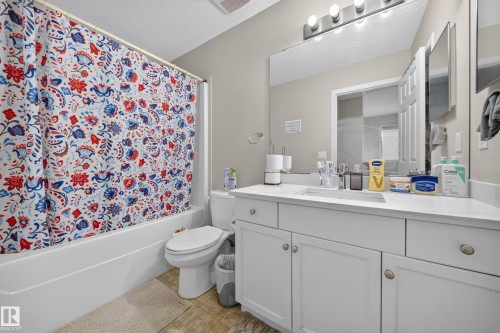 Full bathroom featuring a white vanity with integrated sink, a large wall-mounted mirror, a standard toilet, and a combined shower and bathtub - 59 2503 24 Street, Edmonton, AB 