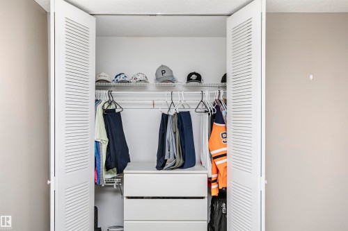 Louvered bi-fold doors reveal a built-in closet system featuring wire shelving, hanging rods, and a white drawer unit - 204 11440 40 Ave, Edmonton, AB 