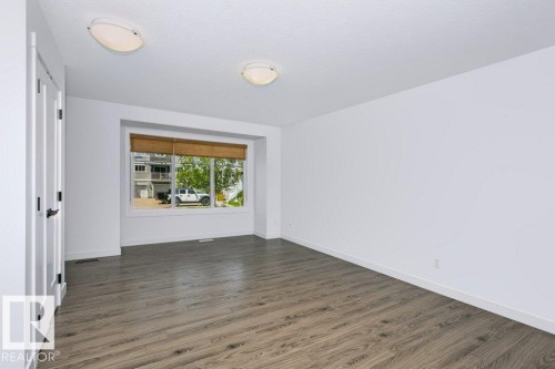 Spacious room featuring wood-finish flooring, white baseboards, and white walls - 27 4205 30 Street, Edmonton, AB 
