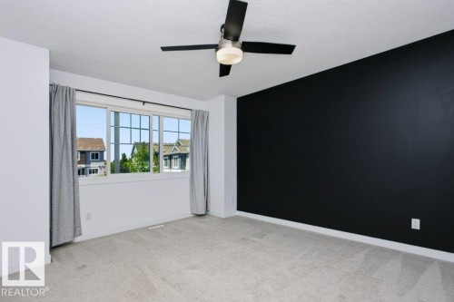 Spacious room featuring a large window, a black accent wall, light-toned carpeting, and a ceiling fan with integrated lighting - 27 4205 30 Street, Edmonton, AB 