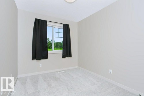 Carpeted room featuring a window with exterior grilles, neutral wall paint, white trim, and an overhead flush-mount light fixture - 27 4205 30 Street, Edmonton, AB 