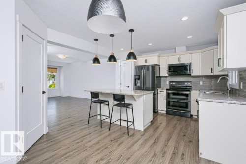 Modern kitchen featuring stone countertops, stainless steel appliances, a tile backsplash, and wood-finish flooring - 27 4205 30 Street, Edmonton, AB 