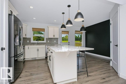 Spacious kitchen featuring an expansive island with a light-toned countertop, white cabinetry, a dark grey subway tile backsplash, stainless steel appliances, and wood-finish flooring - 27 4205 30 Street, Edmonton, AB 