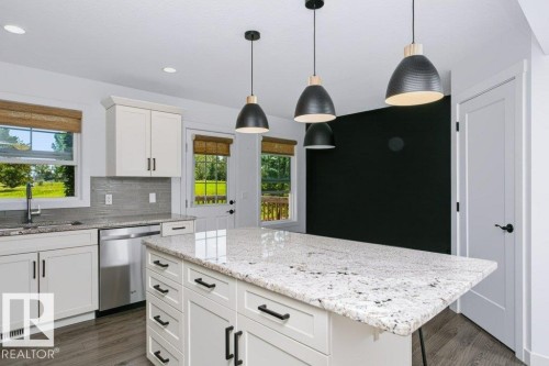 Modern kitchen featuring a large island with a light-toned countertop, white cabinetry with black hardware, stainless steel appliances, and wood-finish flooring - 27 4205 30 Street, Edmonton, AB 