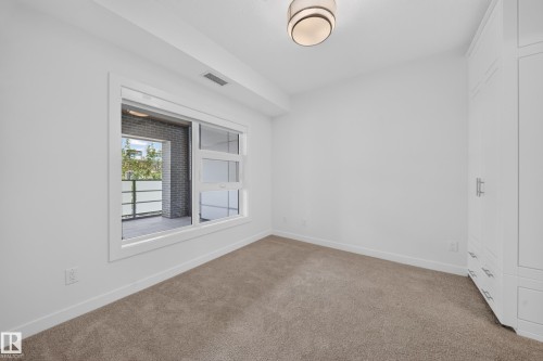 Carpeted room featuring a large window, built-in white cabinetry with chrome hardware, and a modern flush-mount ceiling light - Sherwood Park, AB 