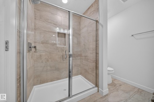 Glass-enclosed shower with stone-finish tile surround, integrated shower niche, and white shower pan - Sherwood Park, AB 