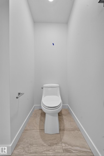 Powder room featuring a sleek white toilet, large format floor tiling, a flush mount ceiling light, and a polished chrome towel bar - Sherwood Park, AB 