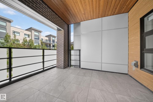 Balcony featuring a wood-panel ceiling, gray tile flooring, brick accent wall, and contemporary railing with frosted panels - Sherwood Park, AB 