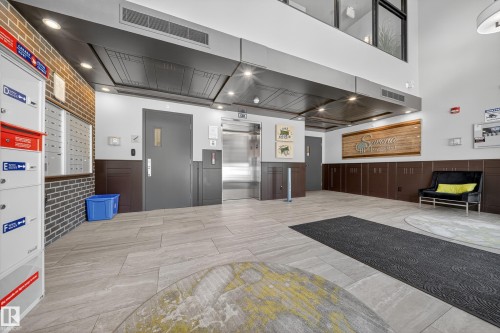 Spacious lobby featuring light-toned tile flooring, a brick accent wall, and a stainless steel elevator - Sherwood Park, AB 
