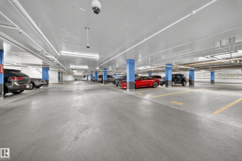 Underground parking garage featuring concrete flooring, blue support columns, overhead fluorescent lighting, and visible ceiling-mounted surveillance cameras - Sherwood Park, AB 
