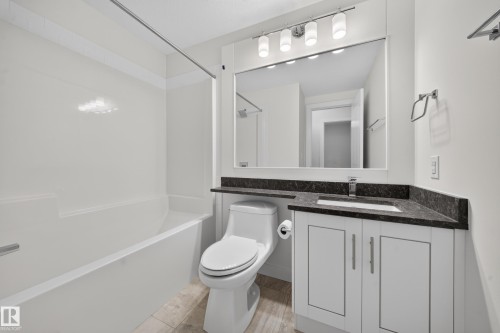 Full bathroom featuring a white tub and shower combination, a single vanity with dark countertop, a rectangular mirror, a chrome-finish light fixture with four cylindrical shades, and tile flooring - Sherwood Park, AB 