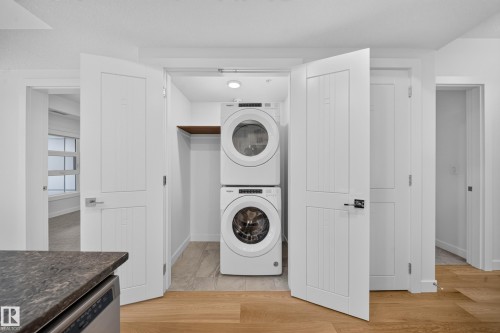 Integrated laundry closet featuring stacked washer and dryer units, a wood shelf, and recessed lighting - Sherwood Park, AB 
