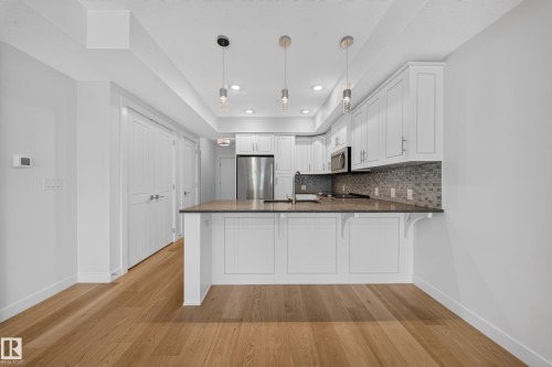 Contemporary kitchen featuring white shaker cabinetry, stainless steel appliances, a mosaic tile backsplash, pendant lighting, and wood-finish flooring - Sherwood Park, AB 