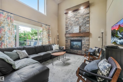 Living area featuring a stone-clad fireplace with a wood mantel, high ceilings, and a large sliding glass door - 1231 Tredger Crest, Edmonton, AB 
