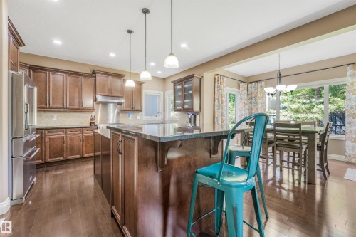 Kitchen with wood-finish flooring, dark wood cabinetry, a center island with a dark countertop, and stainless steel appliances - 1231 Tredger Crest, Edmonton, AB 