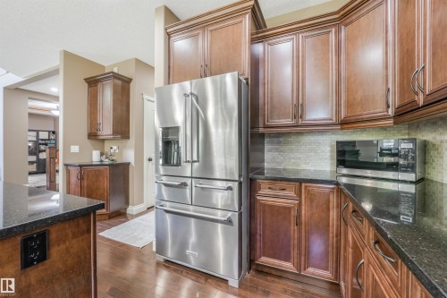 Kitchen featuring wood-finish cabinetry, dark countertops, and a tiled backsplash - 1231 Tredger Crest, Edmonton, AB 