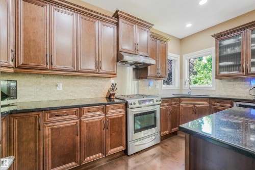 Kitchen featuring wood-finish cabinetry, dark countertops, stainless steel range, and a tile backsplash - 1231 Tredger Crest, Edmonton, AB 