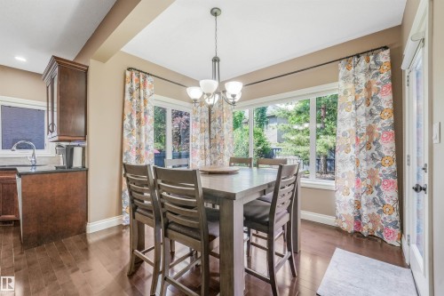 Dining area featuring wood-finish flooring, a contemporary chandelier, and a bay window with a garden outlook - 1231 Tredger Crest, Edmonton, AB 