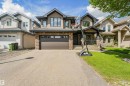 Modern two-story stucco and stone exterior featuring a two-car garage with a brown door, dark-framed windows, a covered front entry with dark railings, and a concrete driveway - 1231 Tredger Crest, Edmonton, AB 