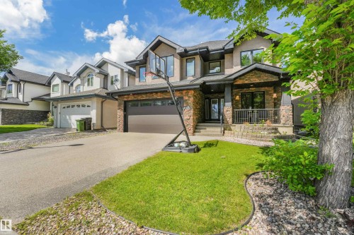 Contemporary stucco and stone exterior featuring a covered front entry, dark trim windows, and an integrated double garage - 1231 Tredger Crest, Edmonton, AB 