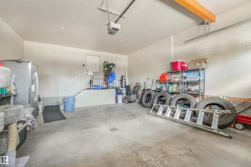 Spacious garage featuring a concrete floor, painted white walls, an internal staircase with white railing, and an overhead garage door mechanism - 1231 Tredger Crest, Edmonton, AB 