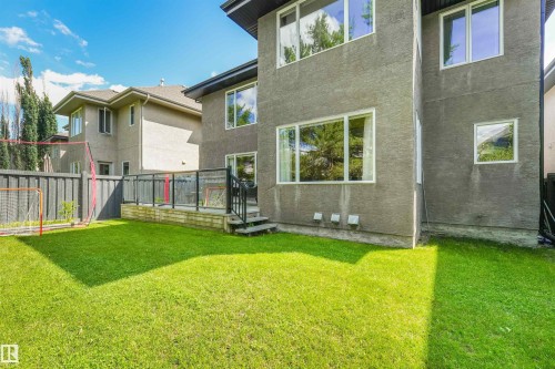 Generous backyard featuring a manicured lawn, an elevated deck with glass railing, and exterior stucco finishes - 1231 Tredger Crest, Edmonton, AB 