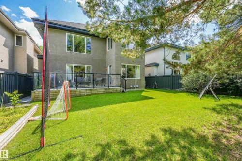 Expansive green lawn with mature trees and a raised deck featuring a glass and metal railing system - 1231 Tredger Crest, Edmonton, AB 