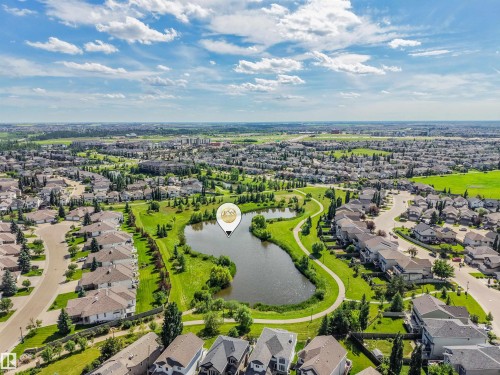 Aerial perspective showcasing a residential area featuring a central pond, green spaces, walking paths, and numerous single-family homes - 1231 Tredger Crest, Edmonton, AB 