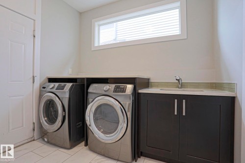 Laundry area featuring a utility sink, dark cabinetry with silver hardware, light-toned countertops, and a horizontal window - 1304 Ainslie Wynd, Edmonton, AB 