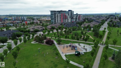 Expansive green space featuring a playground with multiple structures, concrete pathways, mature trees, and surrounding residential properties including multi-story buildings and single-family homes - 1304 Ainslie Wynd, Edmonton, AB 