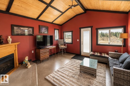 Wood-finish flooring, accent wall with a wood-look finish, exposed beam ceiling, built-in wood-burning stove, and a ceiling fan - 315 57201 Rng Rd 102, Rural St. Paul County, AB 