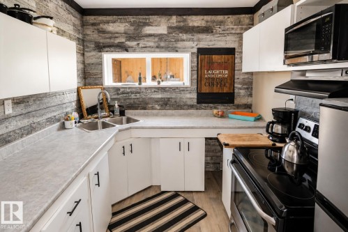 Kitchen featuring light wood-finish flooring, white cabinetry, integrated stainless steel sink, track lighting, and a window - 315 57201 Rng Rd 102, Rural St. Paul County, AB 
