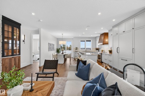 Open-concept living area featuring wood-finish flooring, recessed lighting, a built-in display cabinet with stone surround and wood base, and a contemporary kitchen with light cabinetry, an island, and a wood-hood range - 149 Eastgate Way, St. Albert, AB 