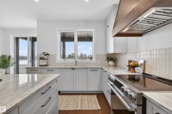 Modern kitchen featuring light gray cabinetry, light-toned stone countertops, and a wood-finish range hood - 